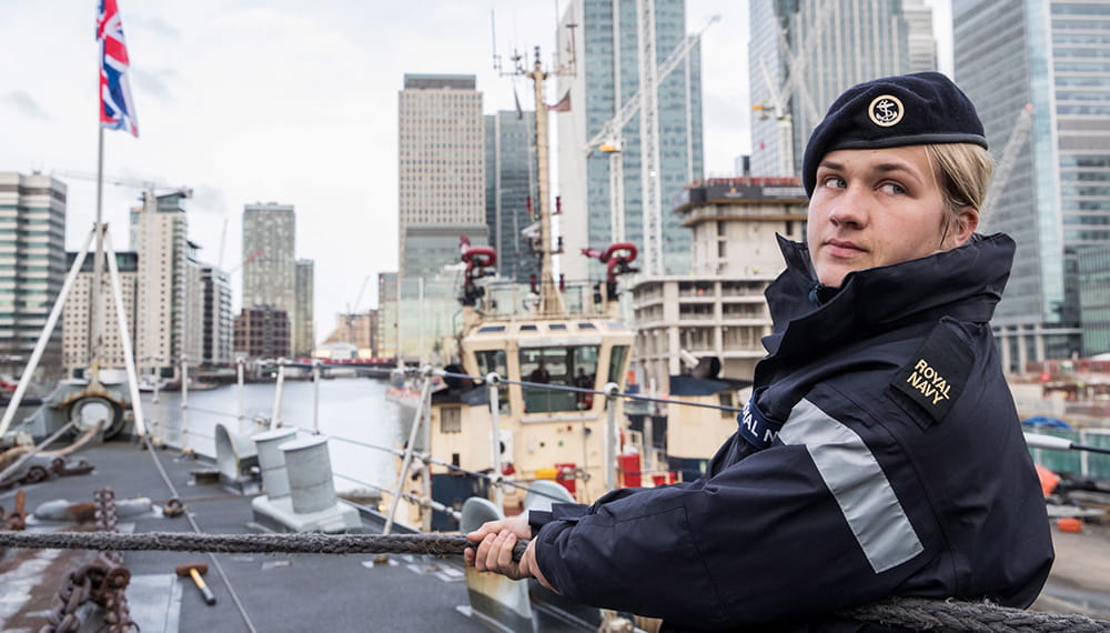 Rating on the deck of ship holding lines with London cityscape in the background