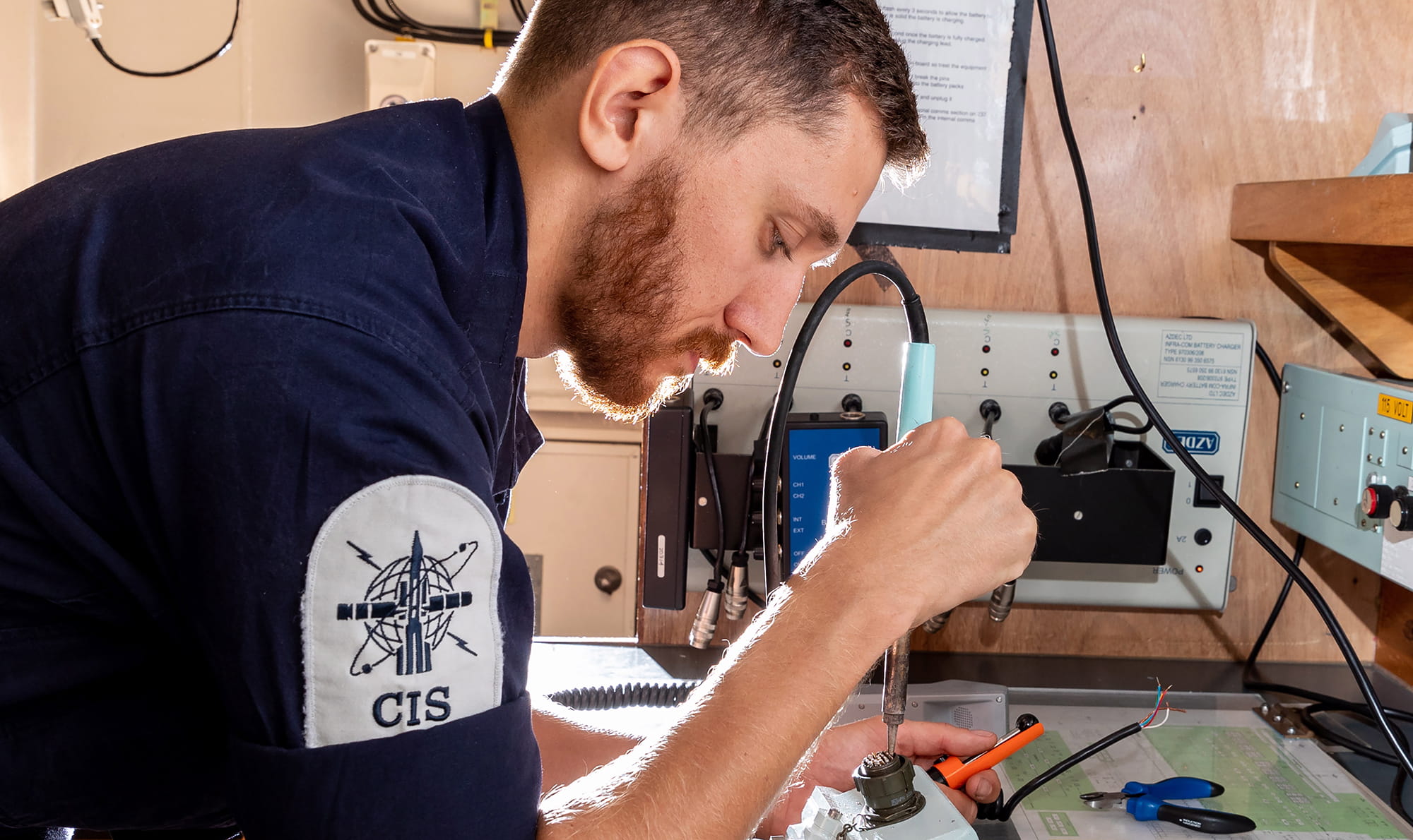 AB ET (Engineering Technician) of HMS Albion, soldering a grey microphone to a new connection for use on a communications user unit
