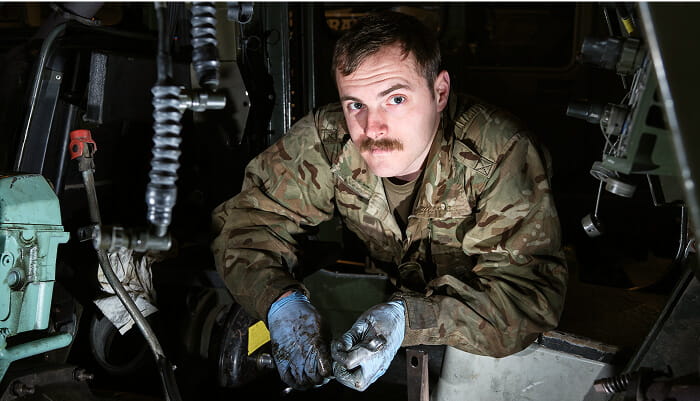 Royal Marine wearing a uniform, with blue gloves and fixing an item, looking directly at the camera.