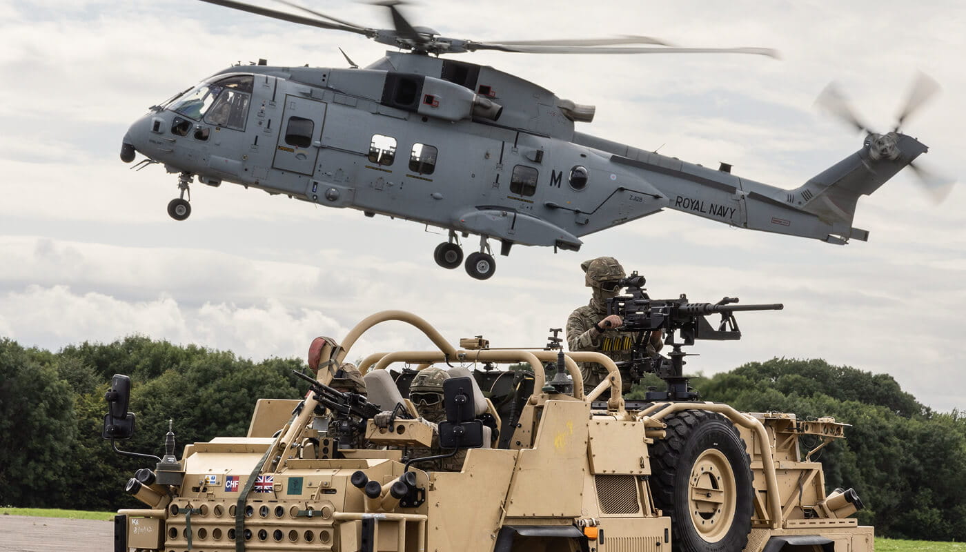An image of a Navy aircraft in the background and two Royal Navy Marines in a vehicle in the foreground.