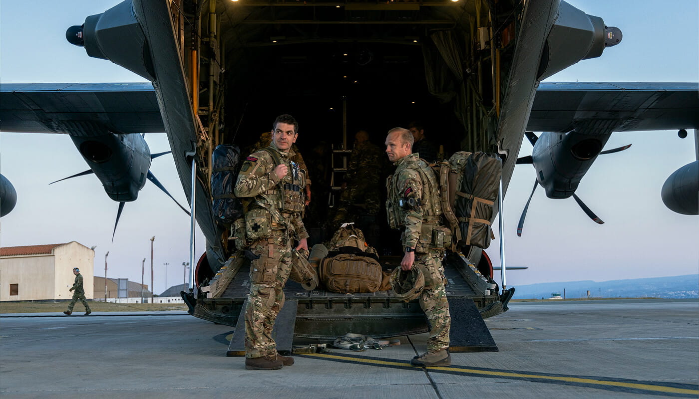 Two Royal Marines at the back of an open parked aircraft on a runway.