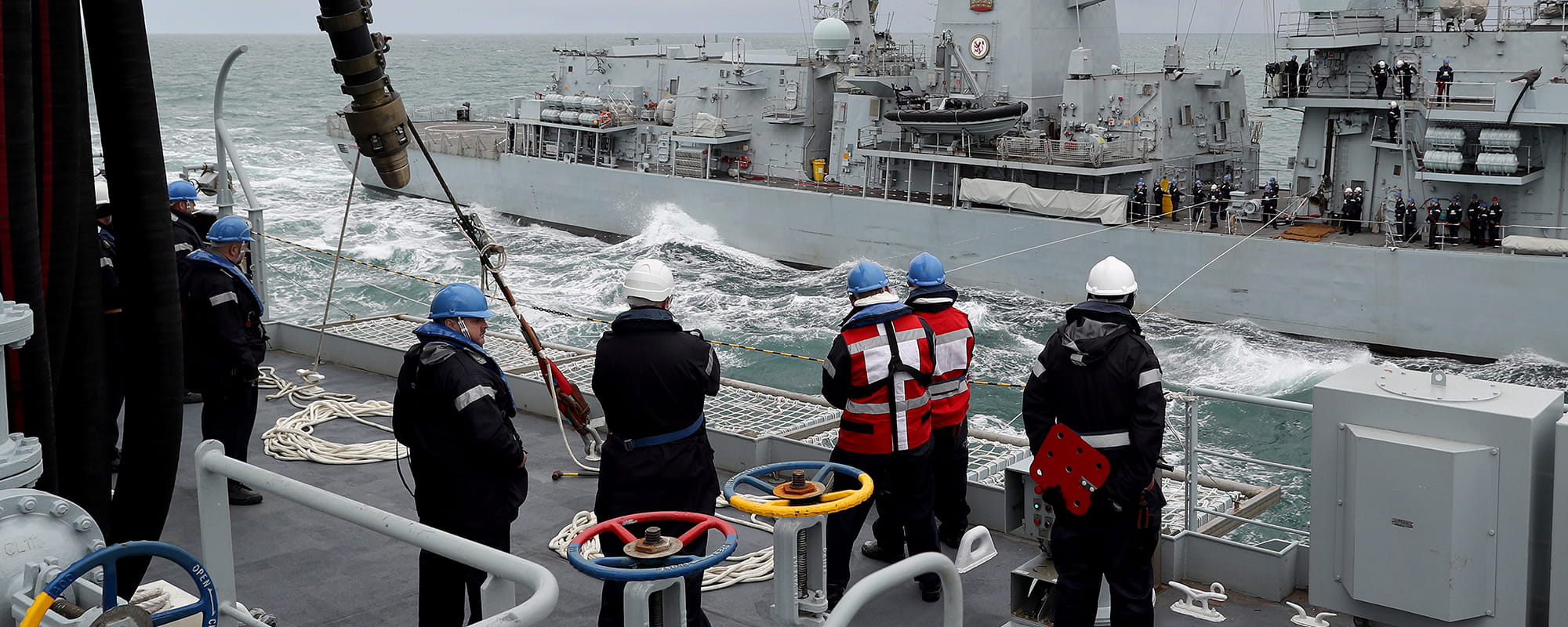 royal-navy-careers-royal-fleet-auxiliary-12 Crew members stand on deck looking at the opposing boat. RFA Tidespring conducts her first ever RAS with a Royal Navy Warship, HMS Sutherland.