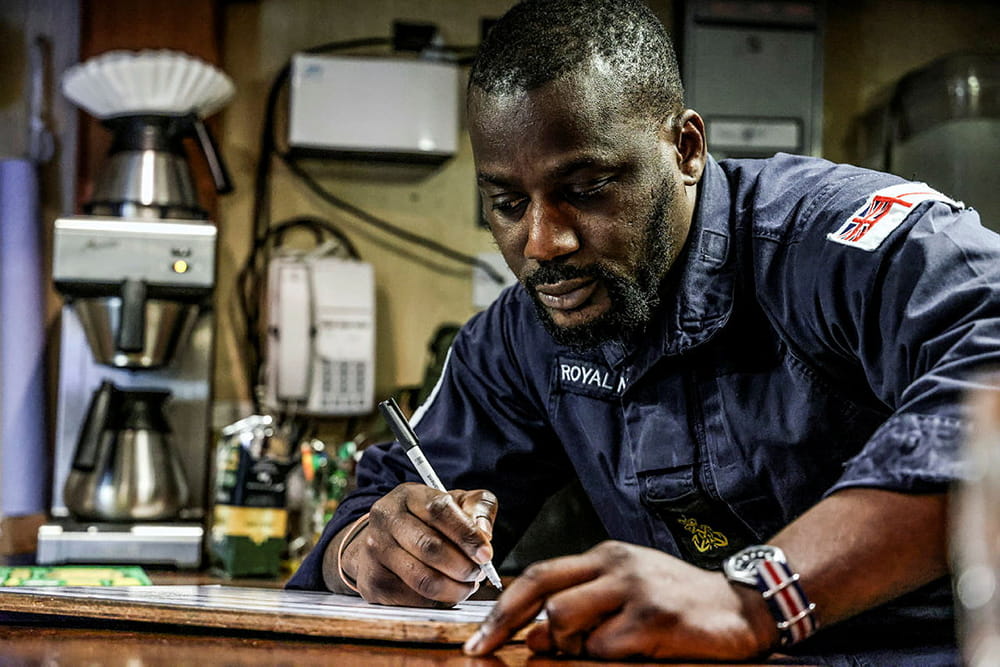 Royal Navy rating sits at the desk writing