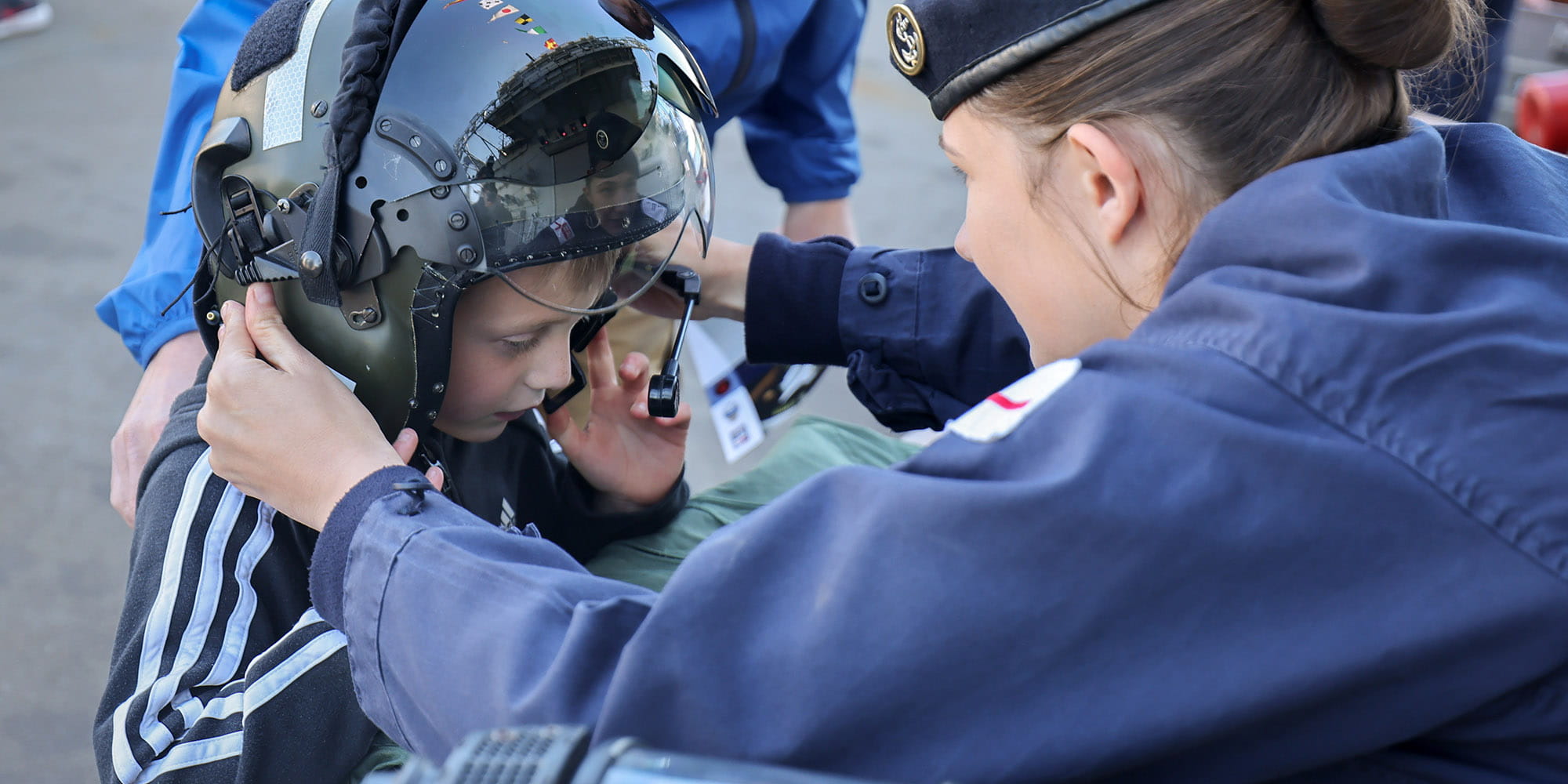 Female service person with back to camera placing crash helmet on young boy