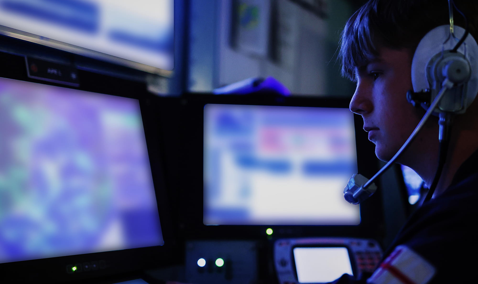 Member of the On Watch Operations Room Team in a dark room in front of blurred-out screens conduct an Air Defence Exercise