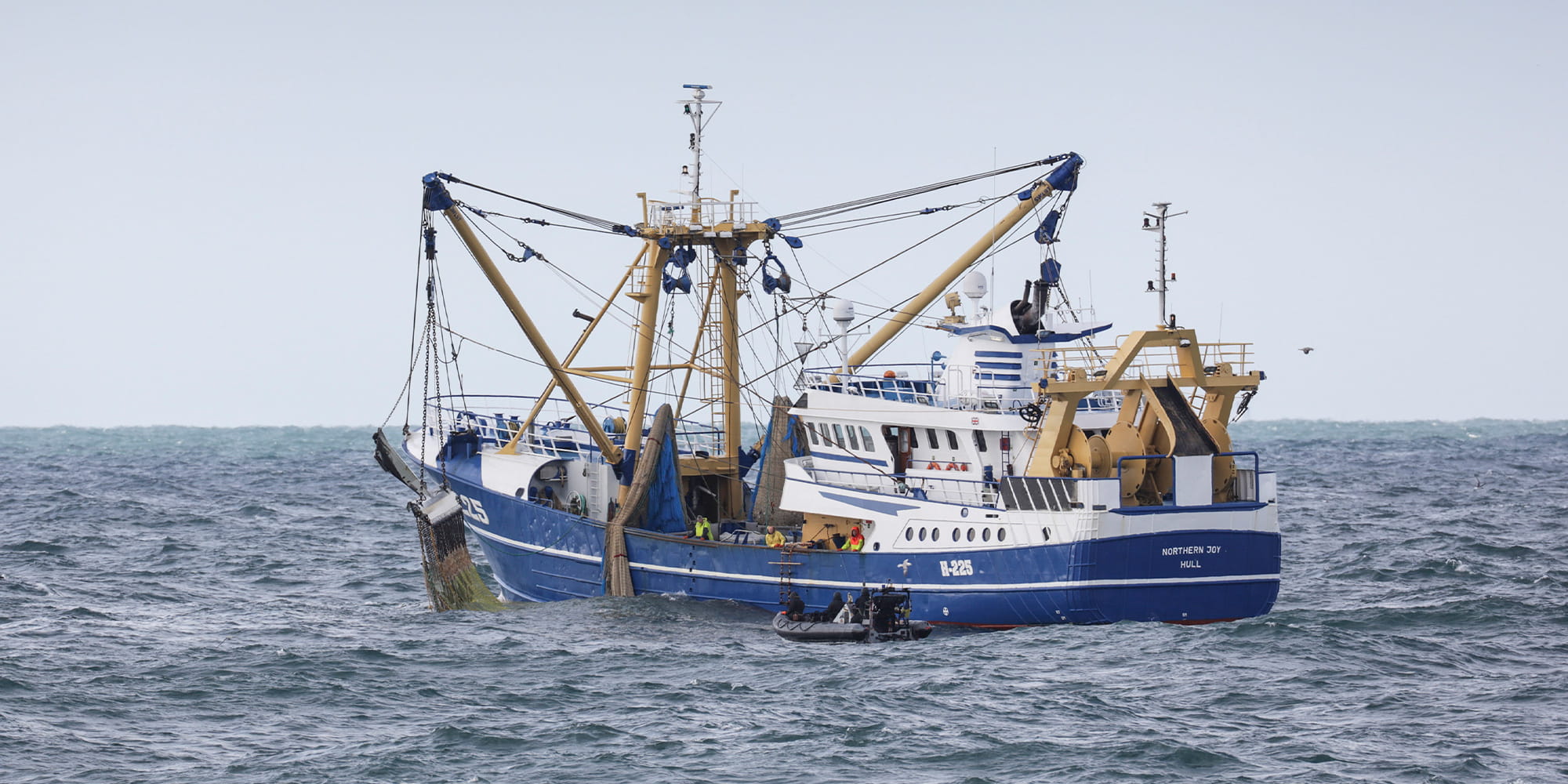 A black rib boat approaches a white and blue fishing vessel on its port side