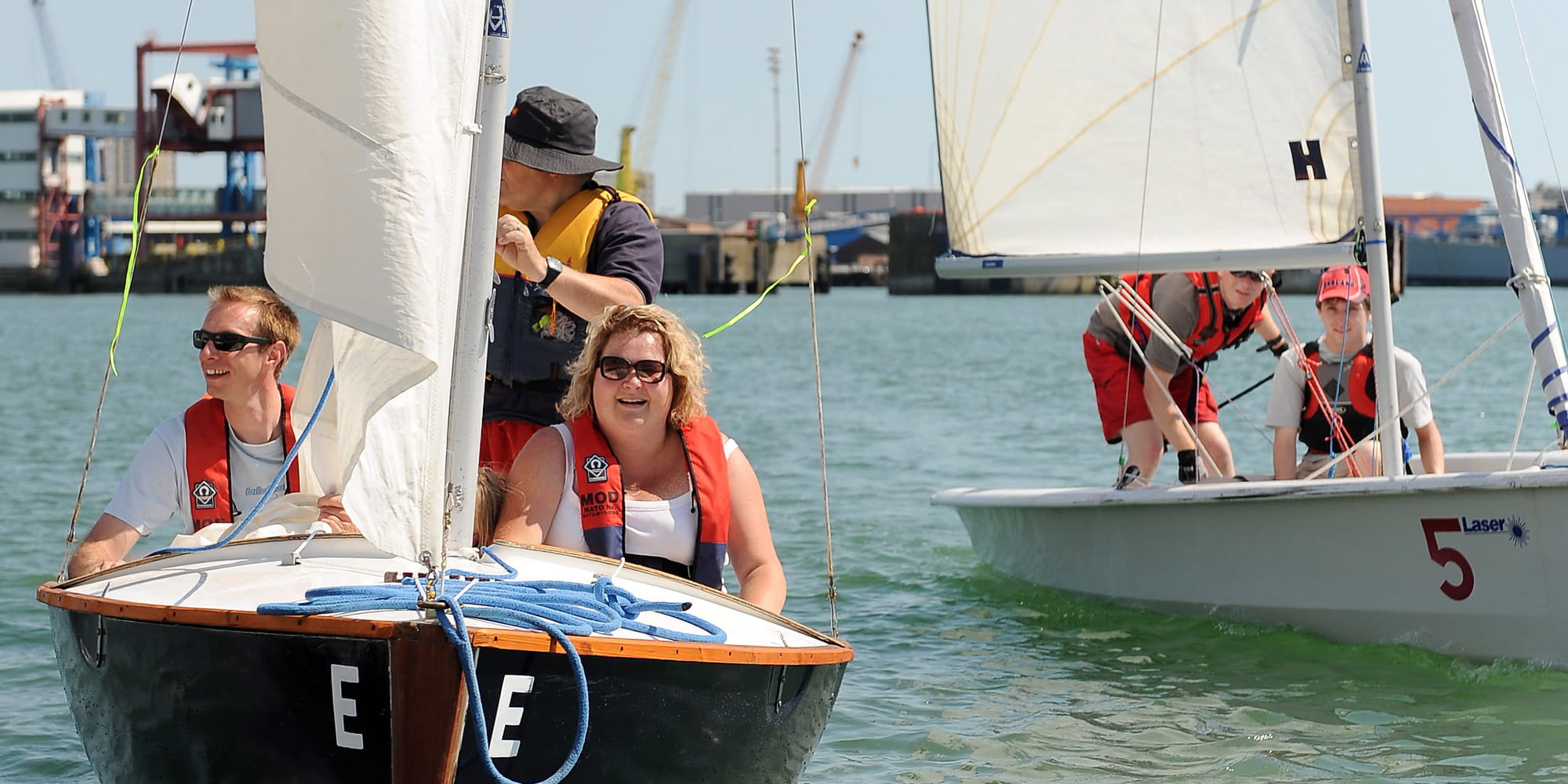 2 small sailing boats with individuals wearing life jackets sailing in port