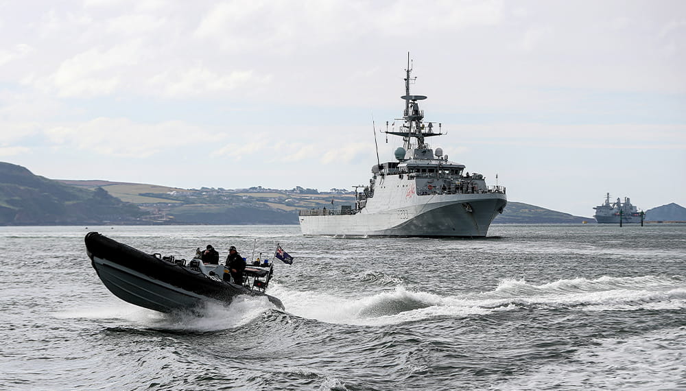 A black rib boats passes at speed in front of HMS Tamar, a River class ship