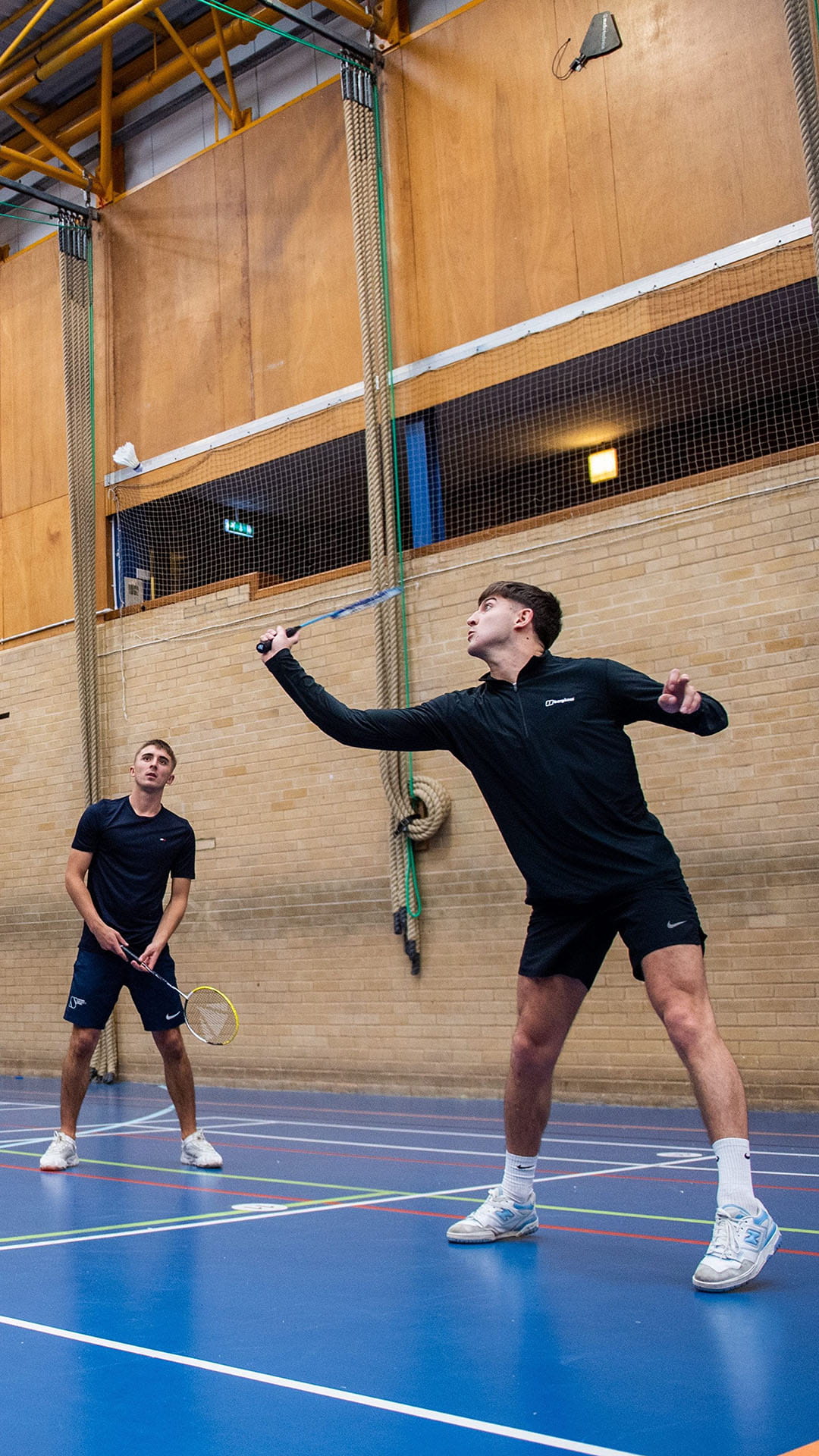 Two people in a badminton court about to hit a shuttlecock