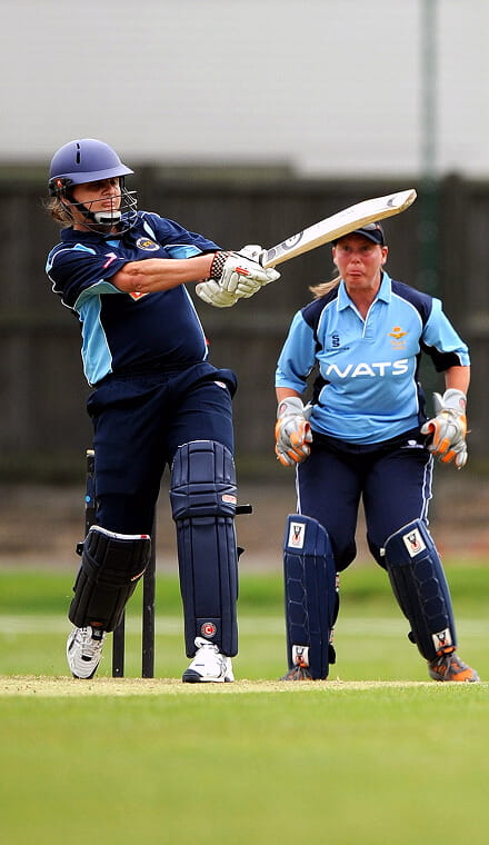 Man wearing a blue cricket outfit and hitting a ball.  An umpire is in the background watching him
