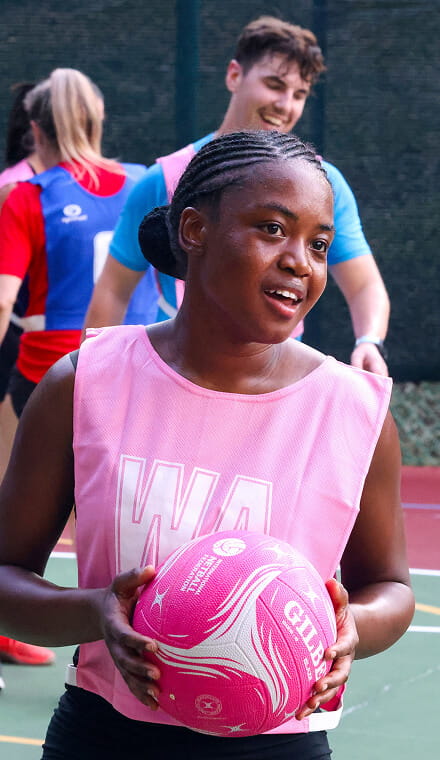 A person wearing a pink netball tabard and holding a pink netball