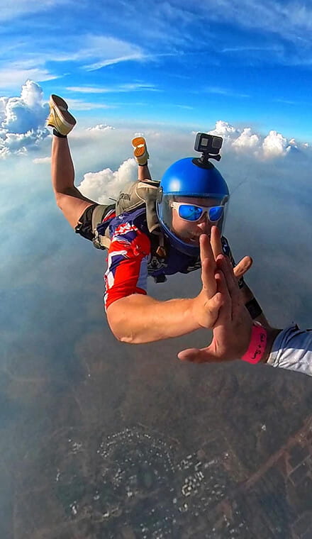 Man free falling while parachuting and holding hands with someone off camera