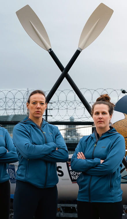 Two women looking at the camera with crossed oars in the background