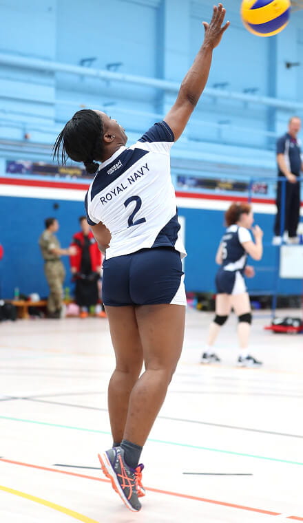 A woman hitting a volleyball over a net with the number 2 on her shirt