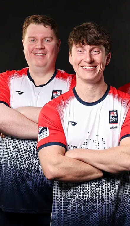 A colour portrait photo shows two Royal Navy esports players. They smile directly at the camera, wearing official Royal Navy esports kit.