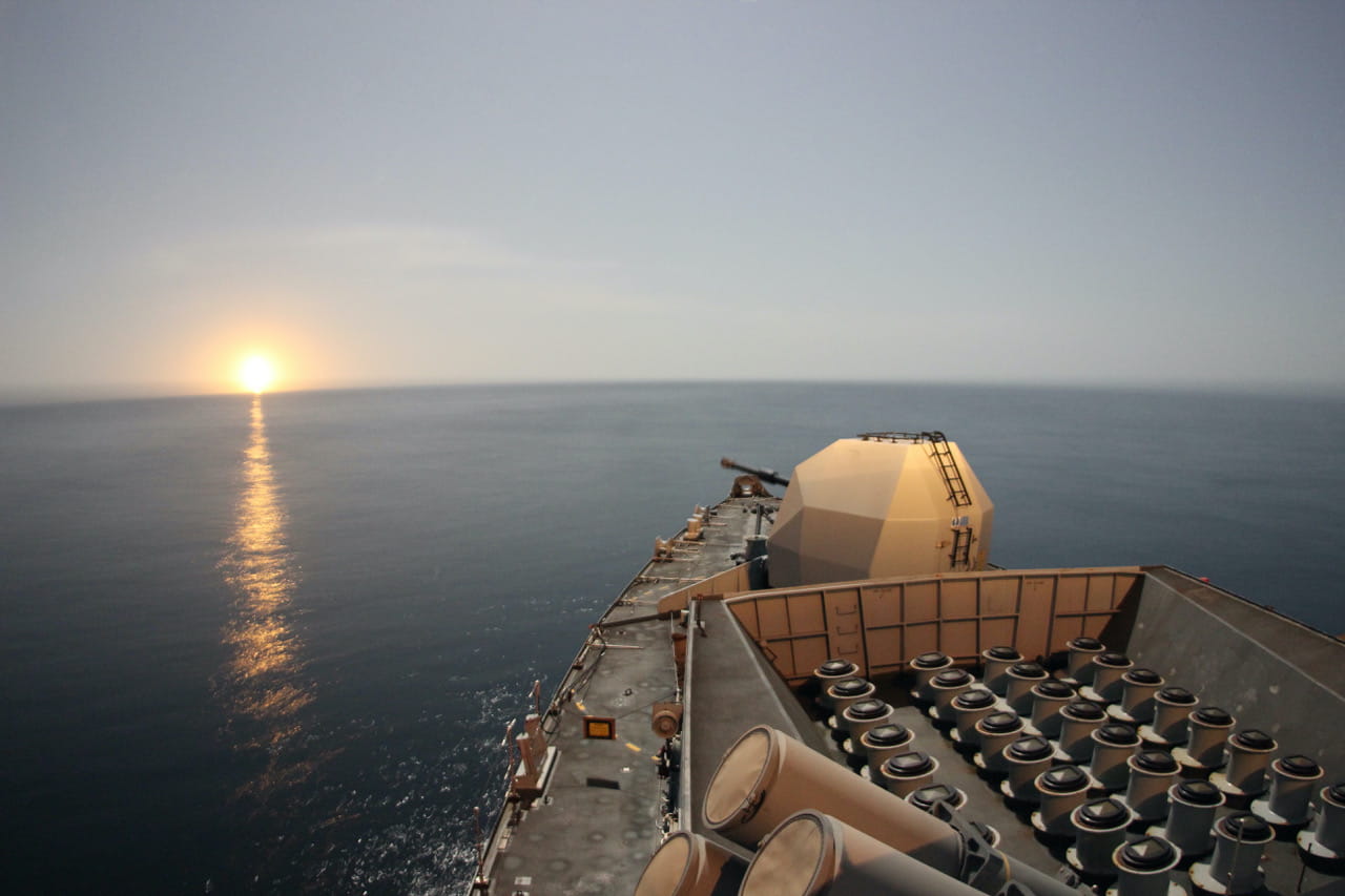 HMS Montrose's bow gleams under a starshell fired as the sun goes down