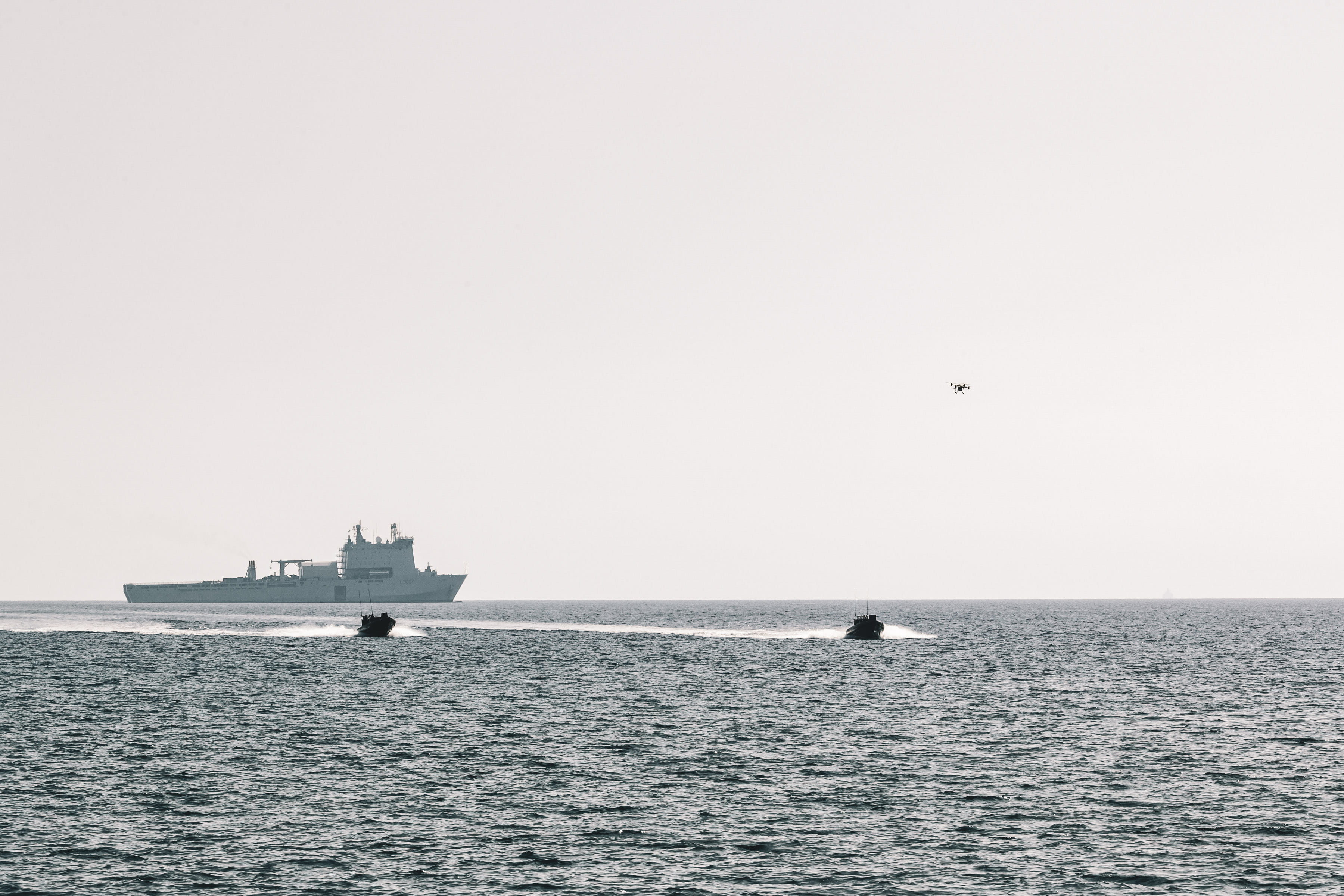 A quadcopter drone passes over RIBs carrying 42 Commando ashore from RFA Lyme Bay in the background