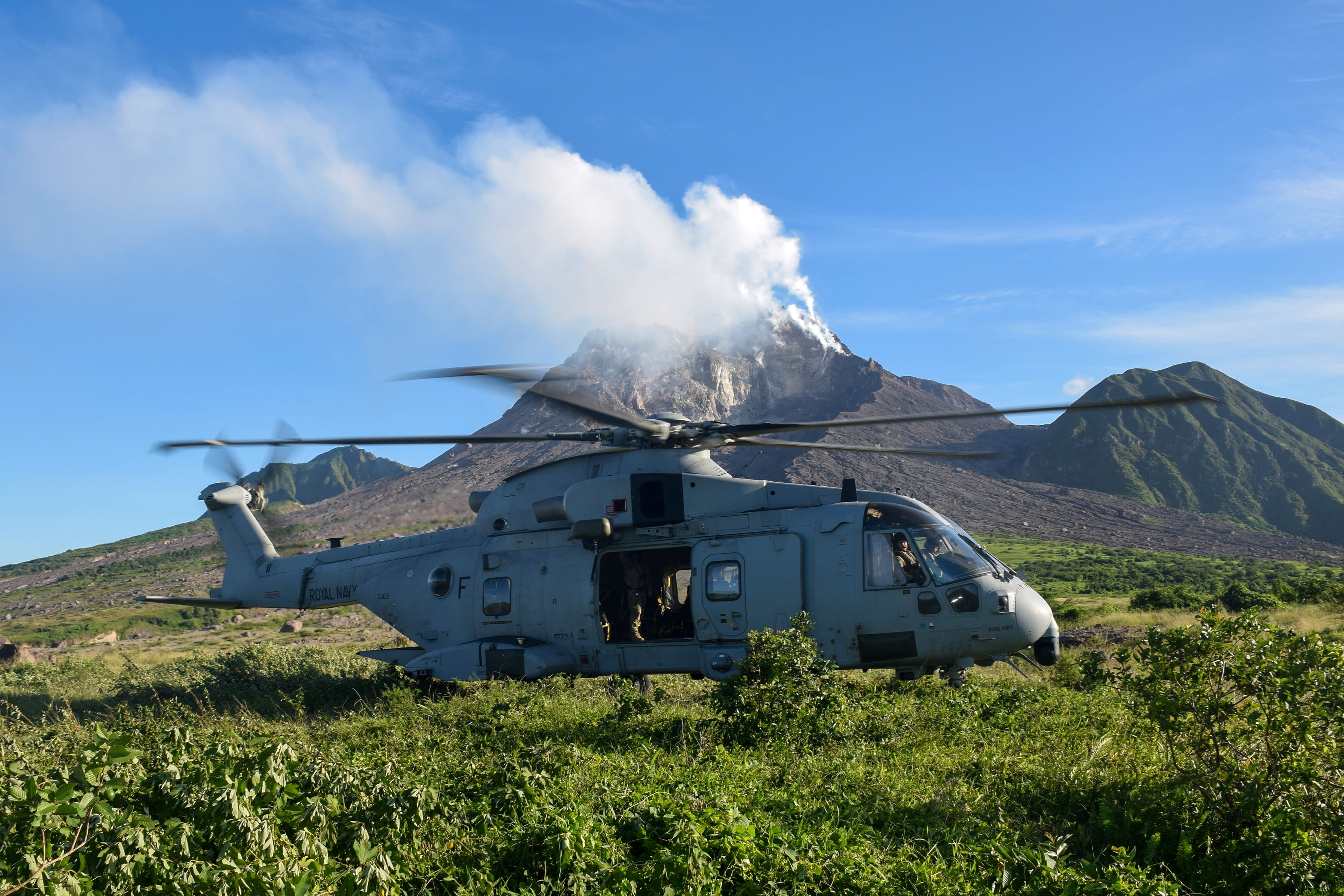 A Merlin Mk4 of 845 NAS lands in Montserrat's exclusion zone with the smoking volcano in the background