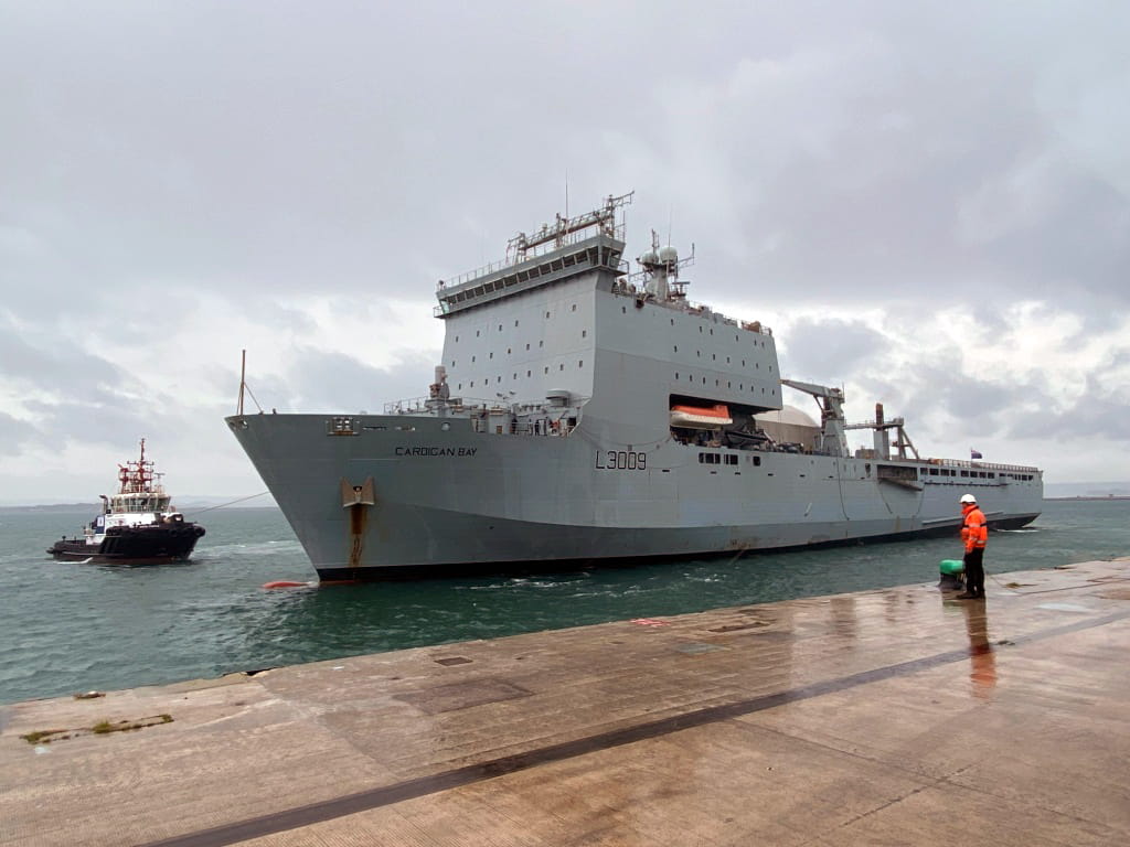A dockyard worker at Portland waits on the damp jetty for Cardigan Bay to berth