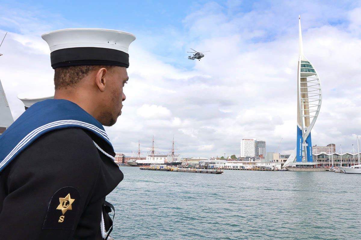A sailor stands to attention as HMS Daring sails home and the ship's helicopter flies past Spinnaker Tower