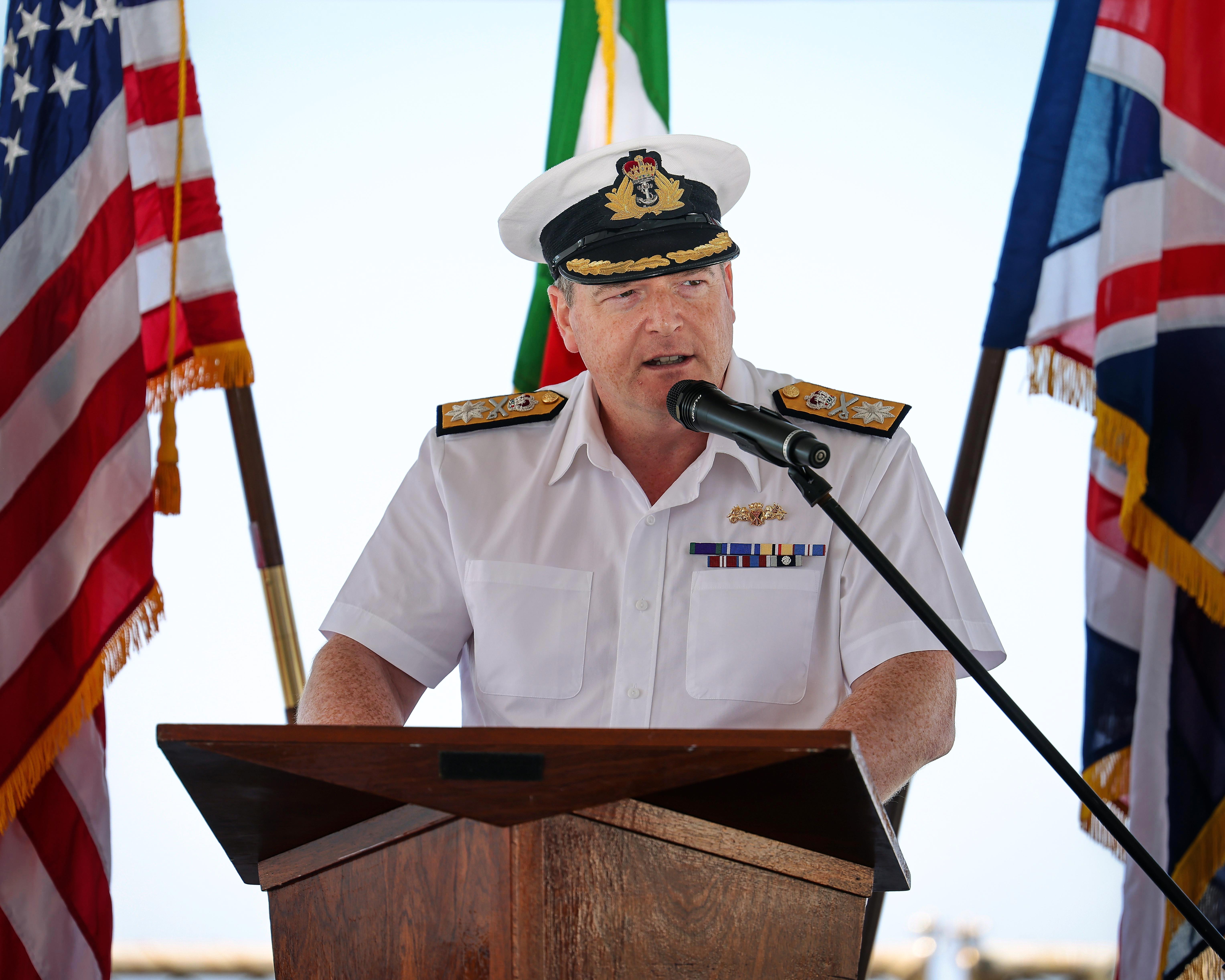Flanked by the US and UK flags, new SNMG2 Commander Cdre Paul Stroude address guests at the handover ceremony