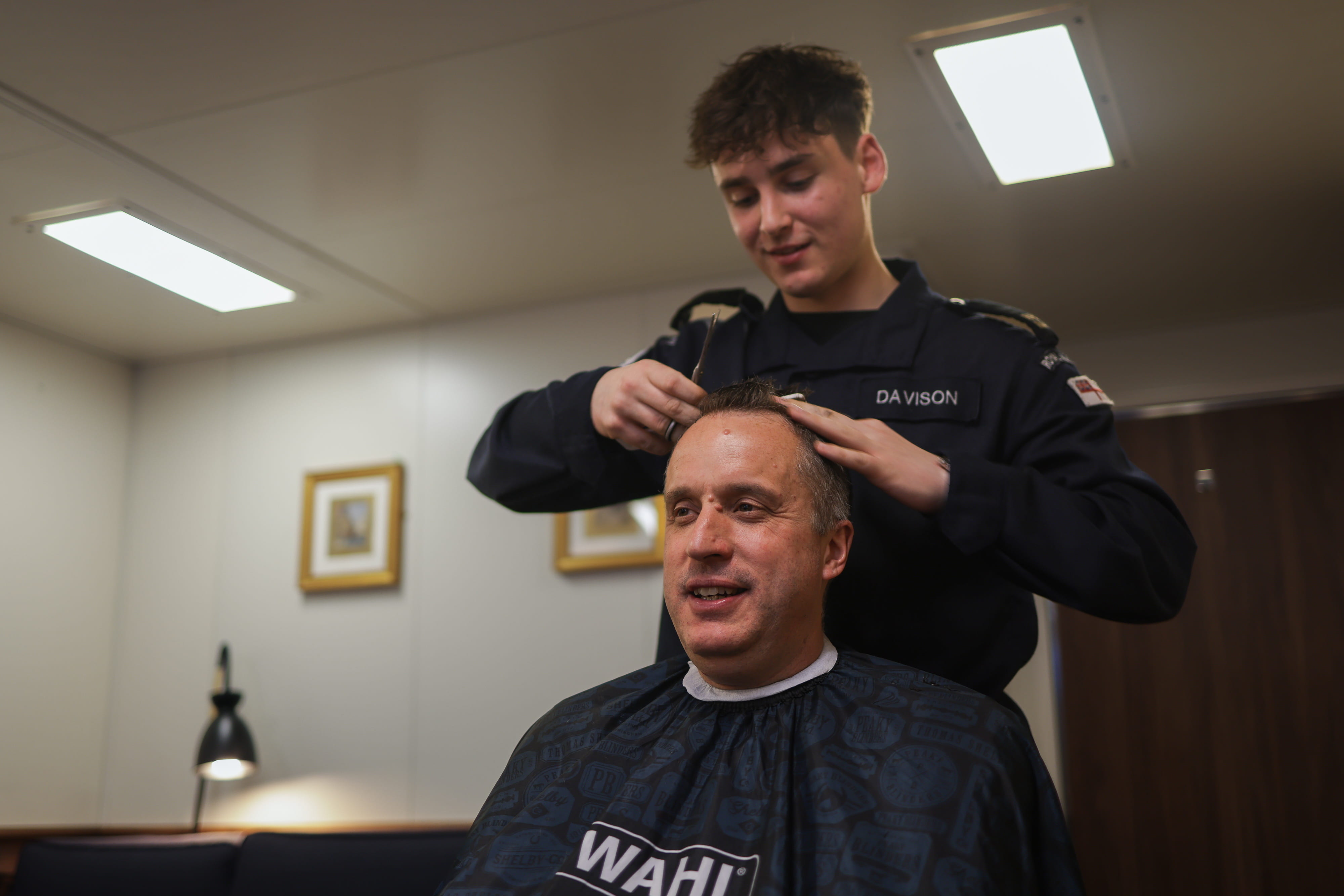 Commodore James Blackmore receives a Finn trim in his cabin aboard HMS Prince of Wales