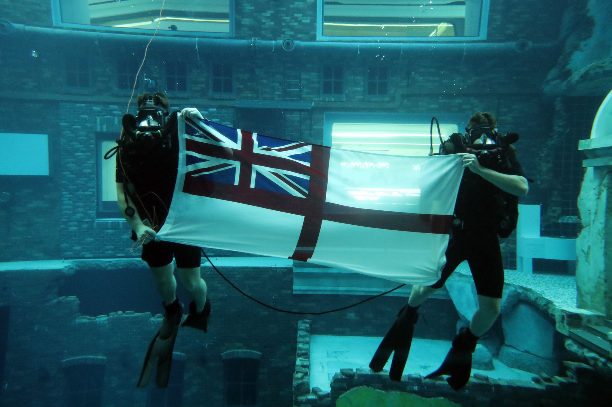 The divers unfurl the White Ensign in the pool